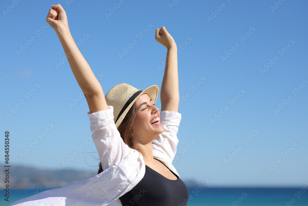 Excited woman with hat celebrating raising arms on the beach Excited woman with hat celebrating raising arms on the beach