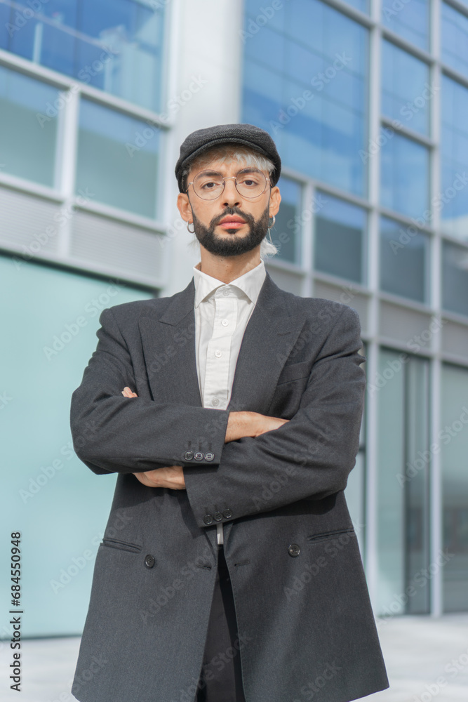 Vertical photo. A young adult businessman posing and looking at camera serious and confident. A cool entrepreneur with glasses and trendy suit looking elegant and smart with arms crossed standing