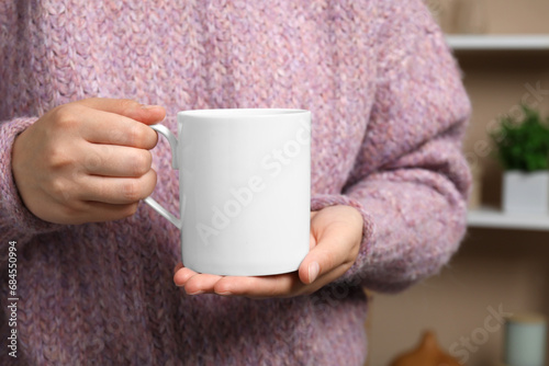 Woman holding white mug at home, closeup. Mockup for design