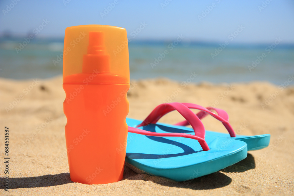 Sunscreen and flip flops on sandy beach. Sun protection care Sunscreen and flip flops on sandy beach. Sun protection care