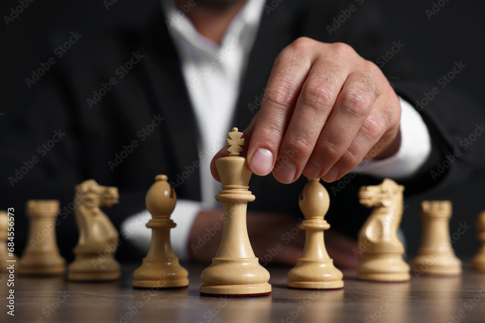 Man with chess pieces at wooden table against dark background, closeup Man with chess pieces at wooden table against dark background, closeup