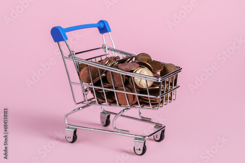 Small metal shopping cart with coins on pink background