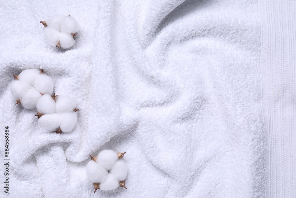 Fluffy cotton flowers on white terry towel, top view. Space for text Fluffy cotton flowers on white terry towel, top view. Space for text