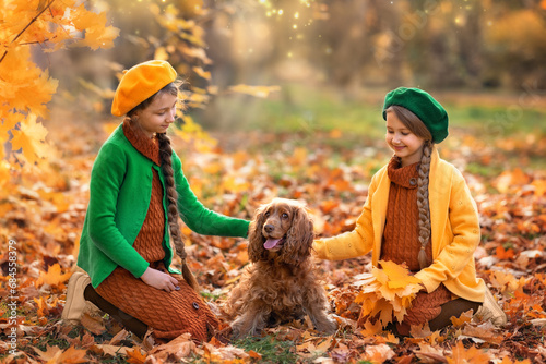 Two little girl children and dog in autumn forest. Female kid and pet portrait at nature with yellow autumn leaves in park during fall outdoor.