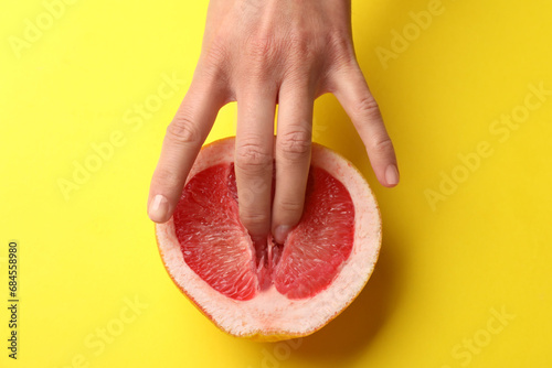 Woman touching half of grapefruit on yellow background, top view. Sex concept photo