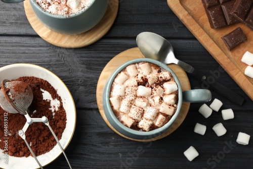 Cups of aromatic hot chocolate with marshmallows and cocoa powder served on dark gray wooden table, flat lay