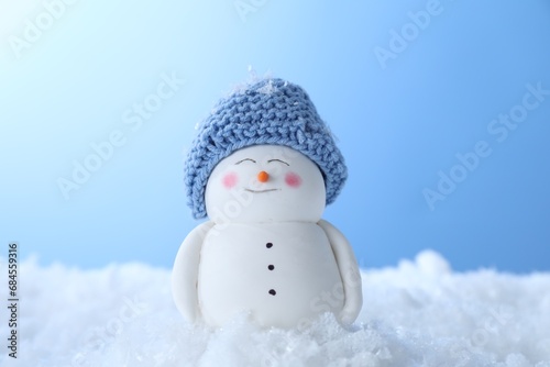 Cute decorative snowman on artificial snow against light blue background, closeup © New Africa