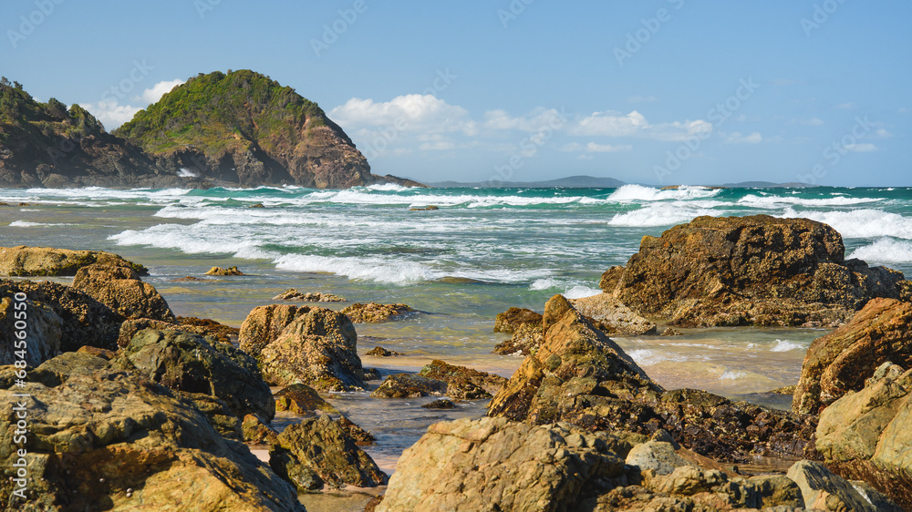 Australian coast with volcanic rocks at the shore, view from the beach to the horizon with blue water with waves on a summer sunny day. Australian coast with volcanic rocks at the shore, view from the beach to the horizon with blue water with waves on a summer sunny day.