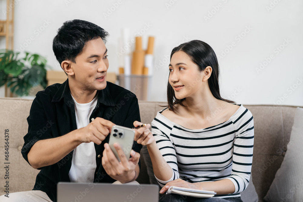 Loving asian family sitting on couch are using credit card payment through smartphone, buying furniture for house, working on design together having conversation.