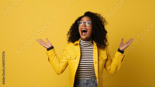 Portrait of excited young woman with curly hair wearing casual yellow jacket celebrating new year with raised hands, raising clenched fists, celebrating victory, photo