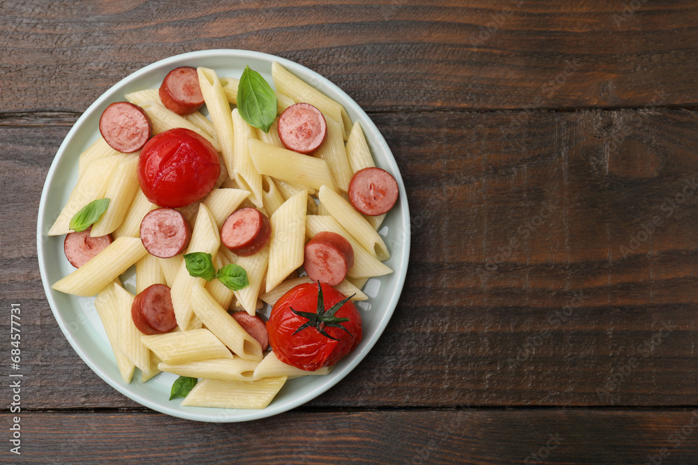 Tasty pasta with smoked sausage, tomatoes and basil on wooden table, top view. Space for text