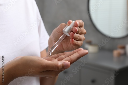 Woman applying cosmetic serum onto her hand indoors, closeup. Space for text