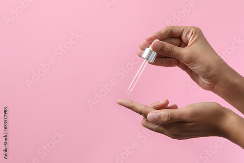 Woman applying cosmetic serum onto her finger on pink background, closeup. Space for text photo