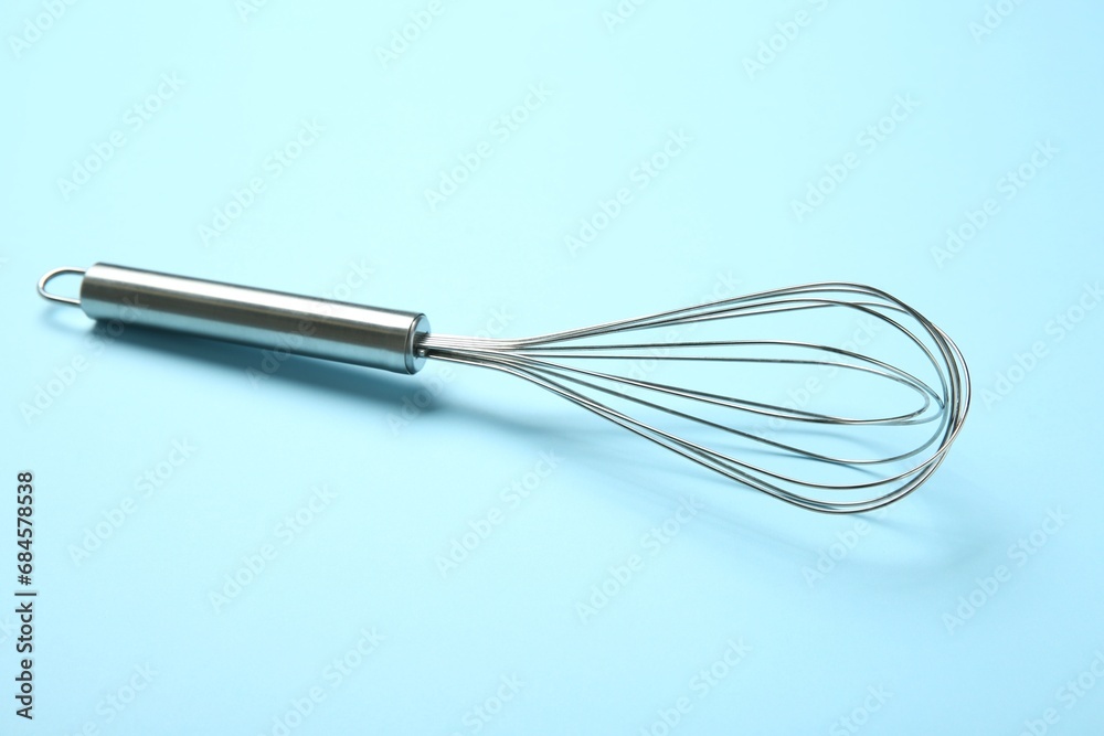 One metal whisk on light blue background One metal whisk on light blue background
