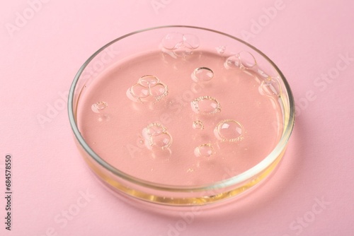 Petri dish with liquid sample on pink background, closeup