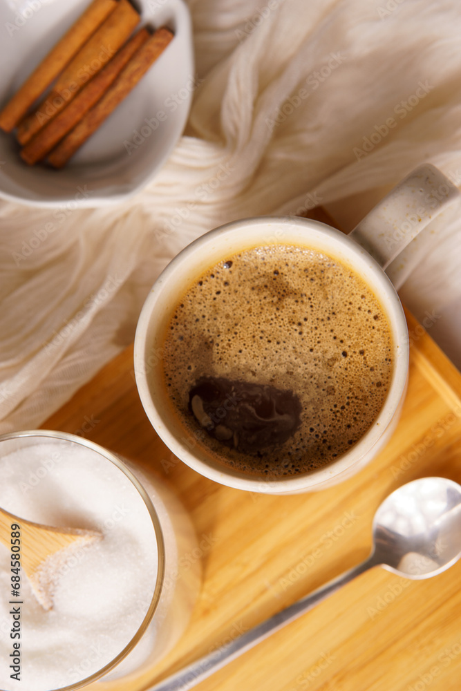 Cup of black coffe served on a white mug. There is a saucer with white sugar on a wooden tray, and everything lays on a white tablecloth. Upside view Cup of black coffe served on a white mug. There is a saucer with white sugar on a wooden tray, and everything lays on a white tablecloth. Upside view