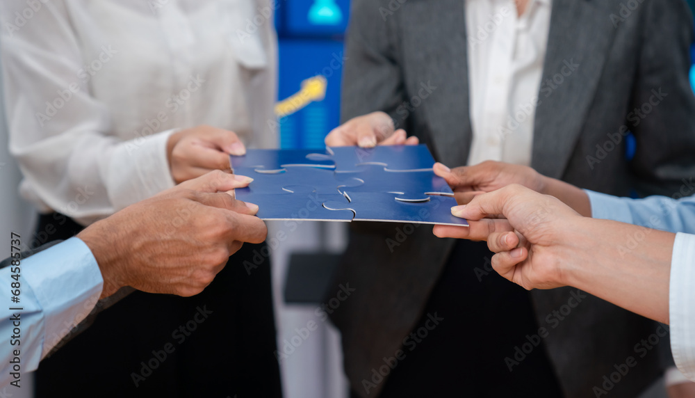 Corporate officer worker collaborate in office, connecting puzzle pieces with report paper on table as partnership and teamwork. Unity and synergy in business concept by merging jigsaw puzzle. Concord