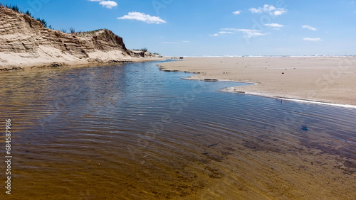 Beach with sand dunes ,river and trees under blue sky with clouds