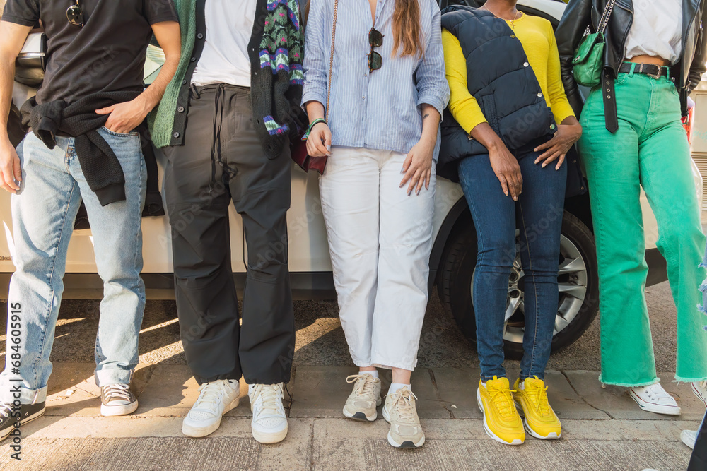 Group of unrecognizable friends standing on road and leaning on car in daylight