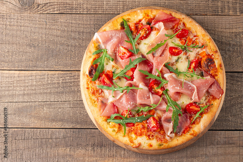 Pizza with prosciutto, ham, arugula, tomatoes, pesto, cheese and parmesan. Italian cuisine. 