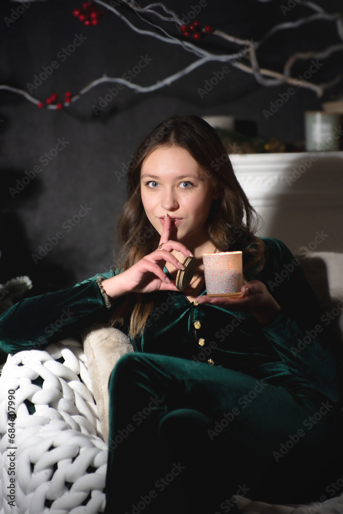 Naklejka premium A girl holds a candle while sitting in a chair in the evening against the background of a fireplace.