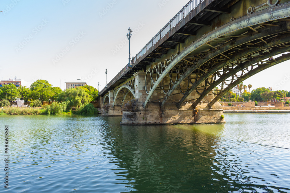 The Puente de Isabel II, Puente de Triana or Triana Bridge, is a metal arch bridge in Seville, Spain, that connects the Triana neighbourhood with the centre of the city. The Puente de Isabel II, Puente de Triana or Triana Bridge, is a metal arch bridge in Seville, Spain, that connects the Triana neighbourhood with the centre of the city.