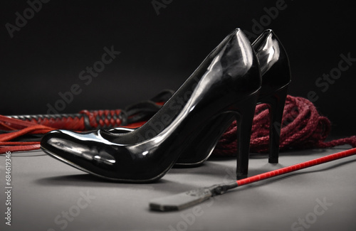 Black shiny high heels, whip and rope stock photo images. Set of erotic toys for BDSM on a dark background. Sexy black high heels and leather flogger. Dominatrix theme still life images