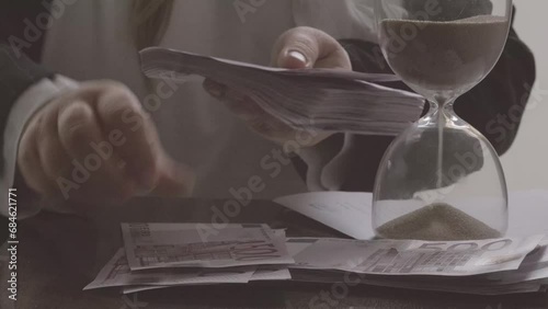 closeup female hands count paper 500 euro banknotes of eu against background of scattered paper banknotes on table, hourglass, concept Time is money, money laundering, financial scam photo