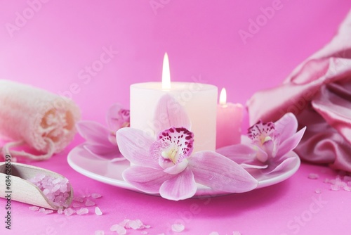 Fresh pink orchid flowers, burning candles, sea salt, on a bright pink background, spa concept, relaxation atmosphere, body care 