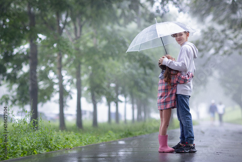 the older brother is carefully hiding his little sister from the rain under an umbrella