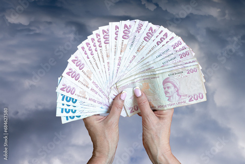 Close-up of female hands holding Turkish lira banknotes on a blue-gray background.