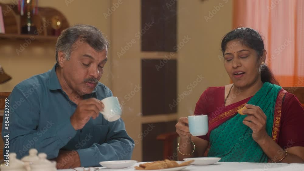 Indian senior couples enjoying morning tea and biscuits at home - concept of healthy morning routine, refreshment and retirement lifestyle
