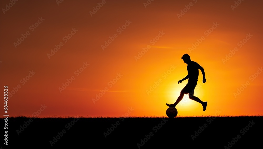 A silhouette of a young football player playing with a ball at sunset.