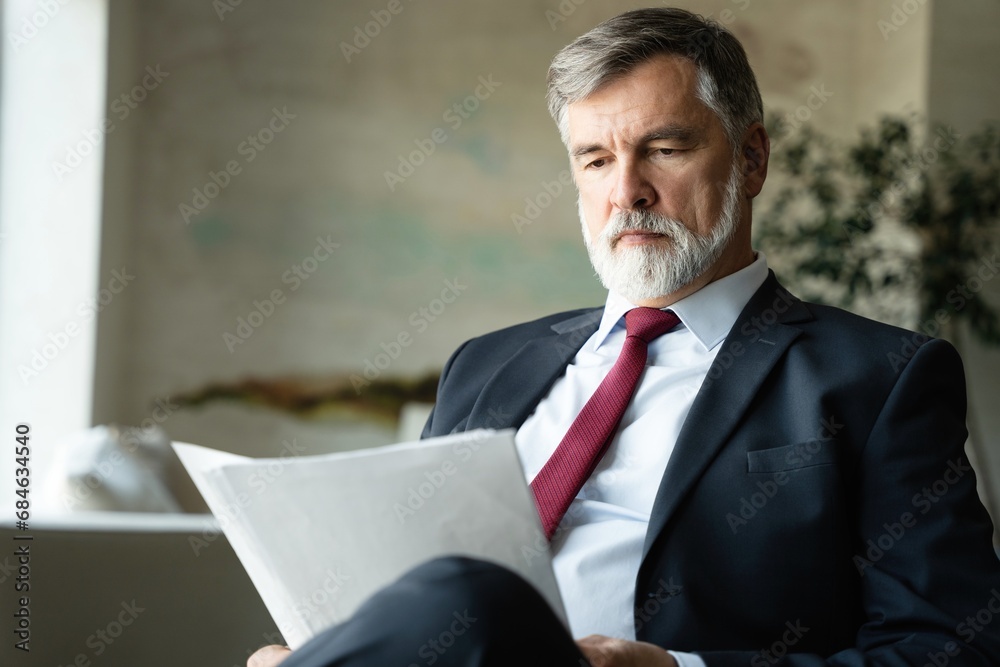 Mature businessman checking and reading documents while working on business project and sitting couch in modern office