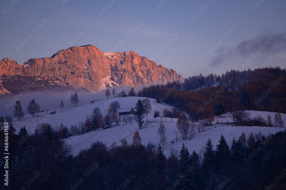 Winter landscape with high and snowy rocky mountains. Amazing sunset in shades of purple in the evening sky