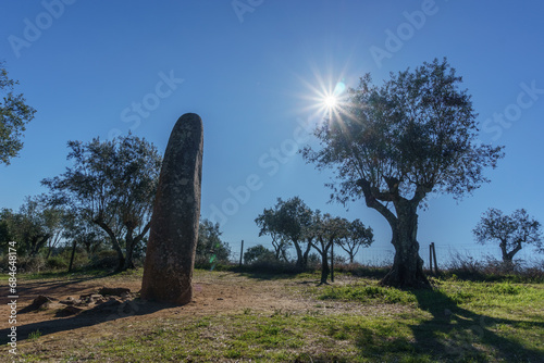 Fotografie Menhir dos Almendres with sun on the blue sky near portuguese town Evora, Alente
