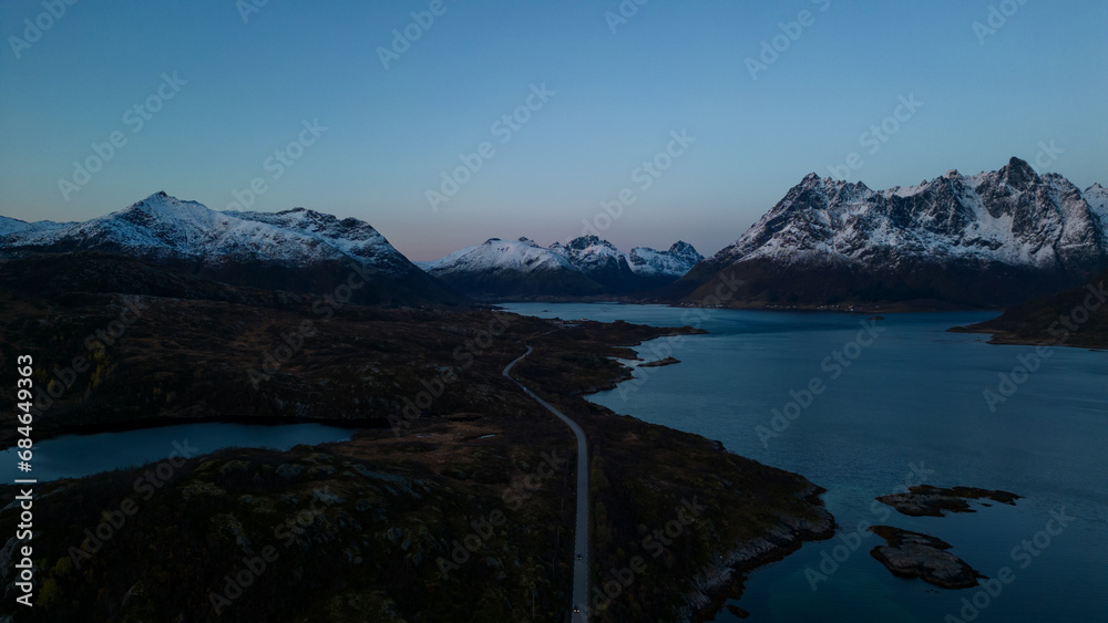 Aerial of highway along fjords in Lofoten, Norway at sunset.  Snow covered mountains captured on image by a drone.  Located far North in the Arctic Circle.