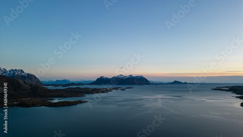 Aerial of highway along fjords in Lofoten  Norway at sunset.  Snow covered mountains captured on image by a drone.  Located far North in the Arctic Circle.