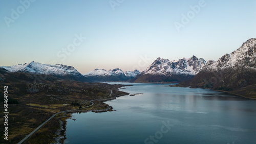 Aerial of highway along fjords in Lofoten, Norway at sunset.  Snow covered mountains captured on image by a drone.  Located far North in the Arctic Circle. © Noah