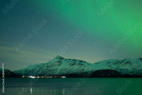 Green Northern Lights Dancing in Arctic skies above a Norweigan lake and mountain.  Beautiful and tranquil Aurora Borealis in the arctic circle in Northern Norway with snowcapped mountains in the back photo