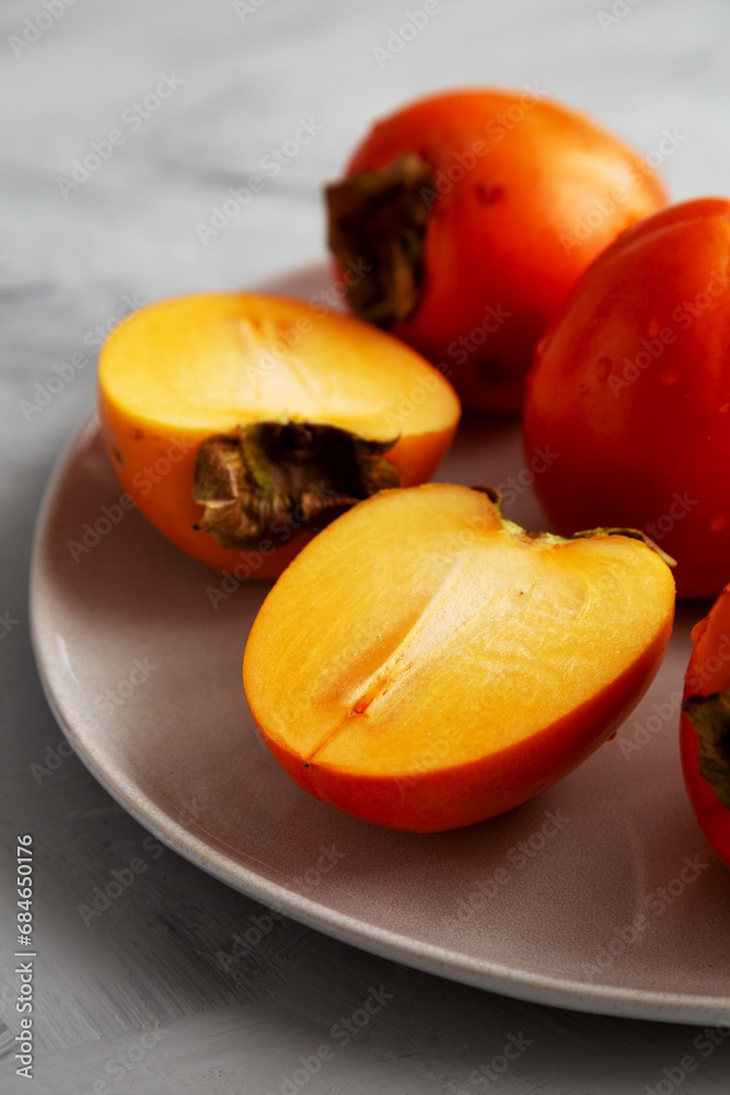 Organic Persimmon Fruit on a Plate on a gray background, low angle view. Close-up. Organic Persimmon Fruit on a Plate on a gray background, low angle view. Close-up.