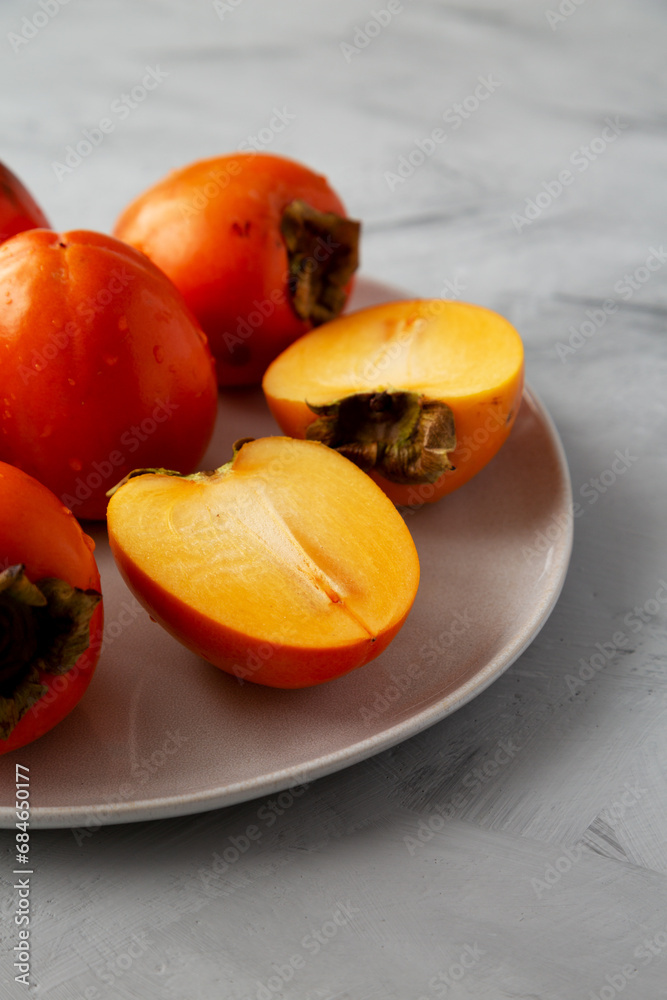 Organic Persimmon Fruit on a Plate on a gray background, low angle view. Close-up. Organic Persimmon Fruit on a Plate on a gray background, low angle view. Close-up.