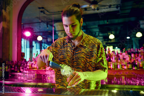 Calm man, bartender preparing ice to making a new sweet tasty cocktail in bar with modern design illuminated neon light. photo