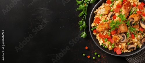 Chicken mushroom paella with vegetables and spices on black bowl top view on concrete table copy space image