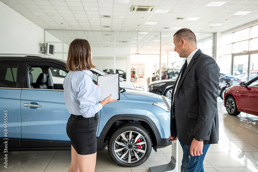 Seller with clipboard and buyer talking about purchase new car in the showroom