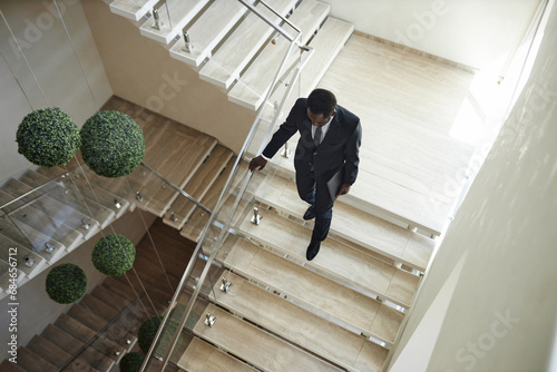 Tableau sur toile High angle shot of African American businessman wearing suit carrying laptop des