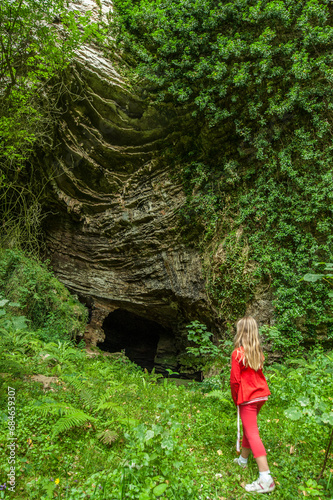Little girl in red at the entrance of a cave