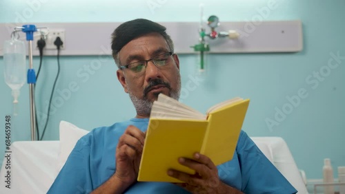 Indian elderly recovered man at hospital reading book at hospital bed - concept of relaxation, medical treatment and contemplation photo