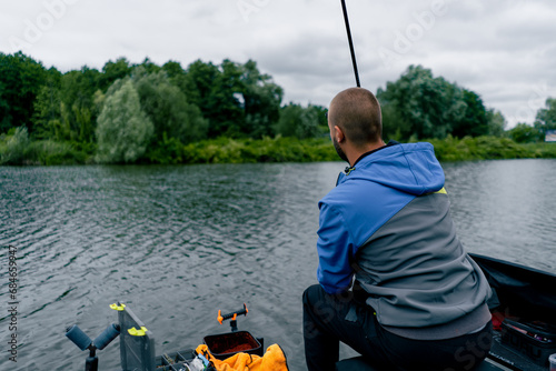 Fisherman with fishing rod or spinning and professional tools sitting on the river bank rear view Pull fish out of the lake sports fishing