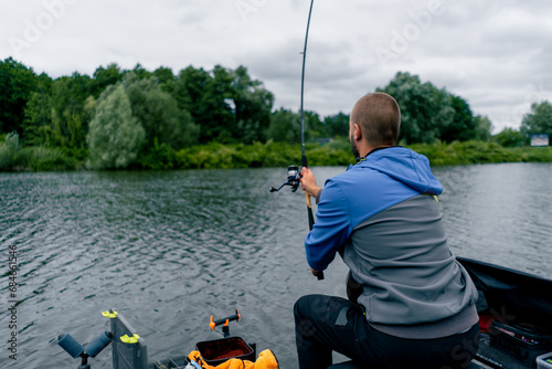 Fisherman with fishing rod or spinning and professional tools sitting on the river bank rear view Pull fish out of the lake sports fishing